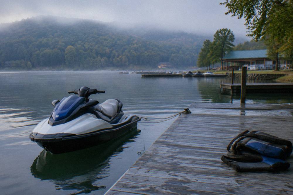 A personal watercraft moored at a wooden dock on a calm cove with wooded hills behind it