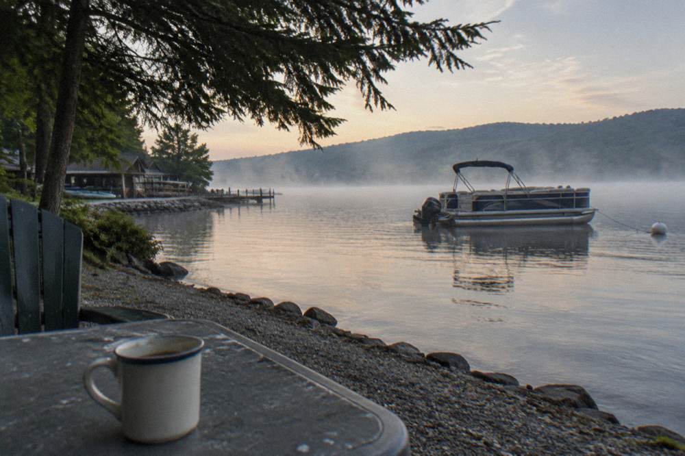 A pontoon boat anchored in a quiet cove with morning mist over the water