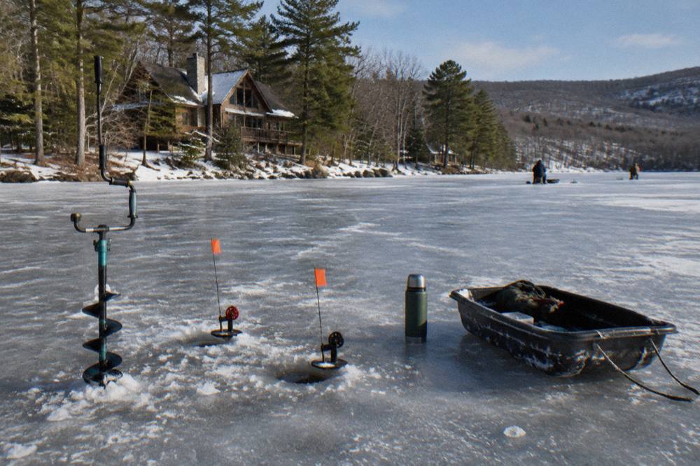 An ice auger and fishing rods set beside holes drilled in a frozen lake surface