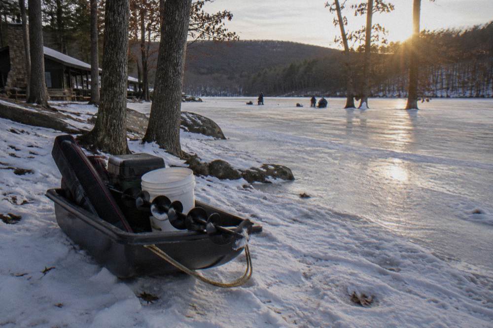 A sled loaded with ice fishing gear resting on snow beside a frozen lake