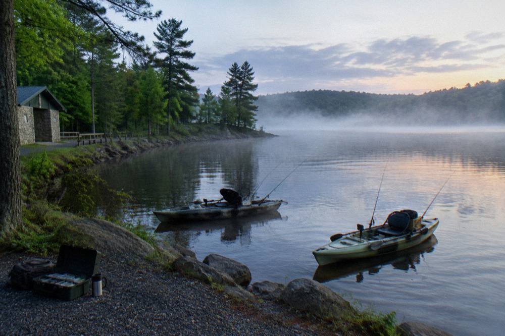 Two kayaks on flat water near a forested point with morning mist over the lake