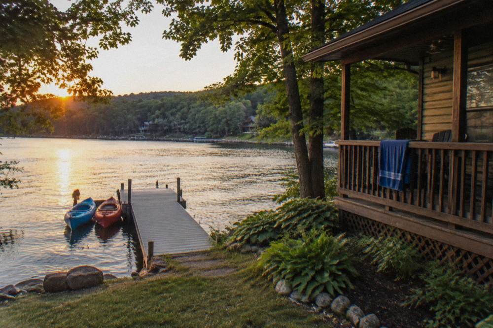 A lakefront cabin with a wooden dock and two kayaks tied at the end of it in evening light
