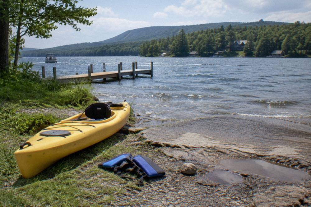 A kayak pulled up on a grassy shoreline beside a rocky public access point on a forested lake