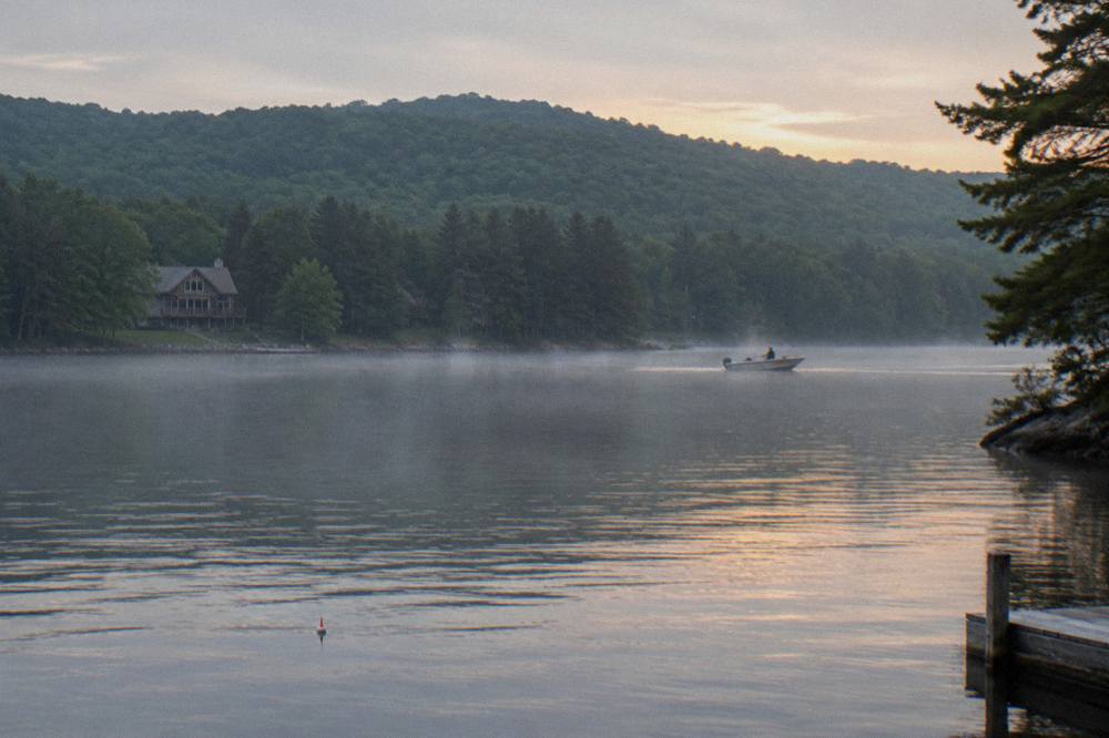 A calm morning on Deep Creek Lake with a forested shoreline and a distant boat