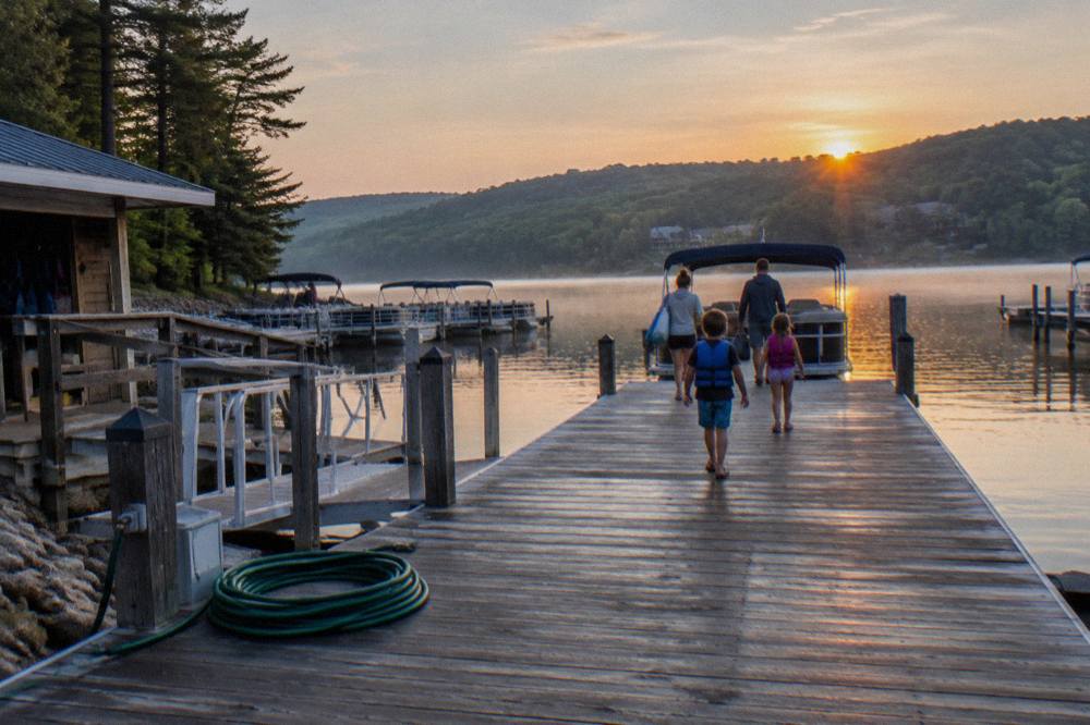 Family walking down a rental dock toward a pontoon boat on a quiet morning lake