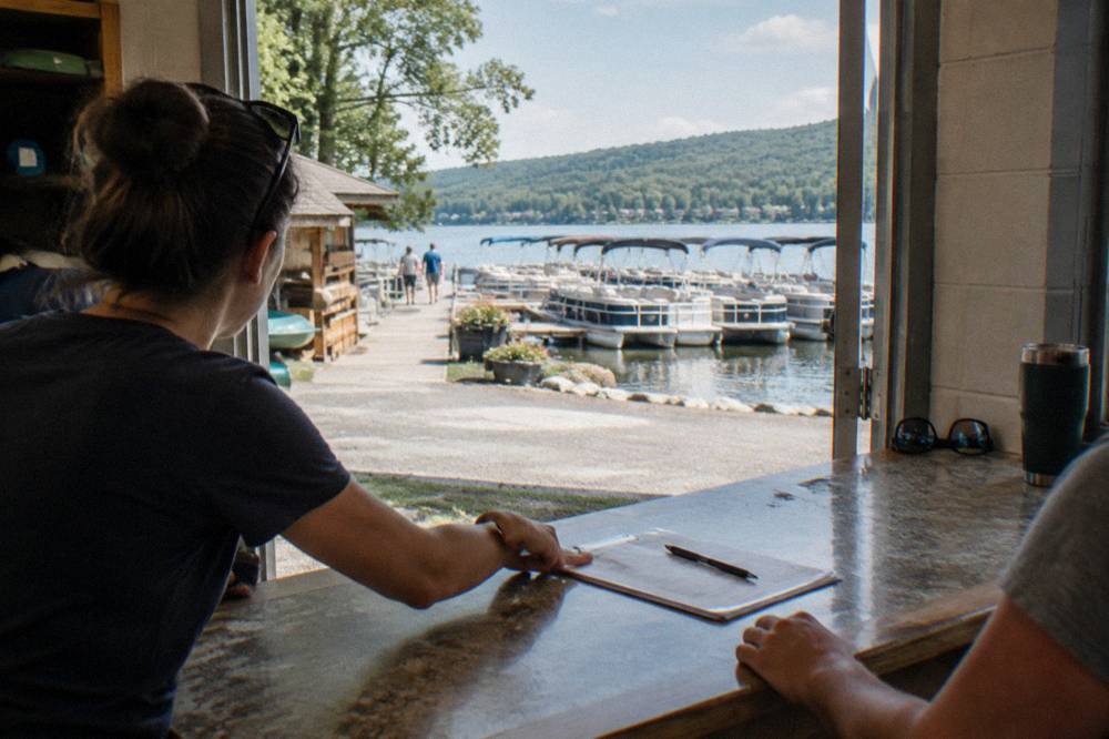 Rental staff handing over paperwork at a marina counter beside rows of pontoon boats