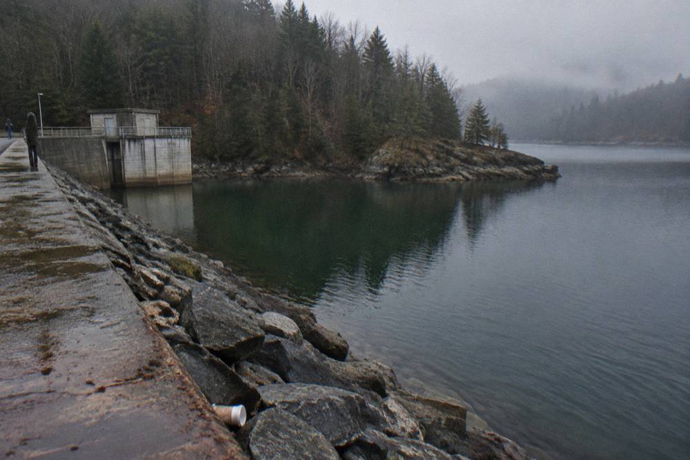Steep forested hillside dropping to deep green water with a rocky point reaching into the lake
