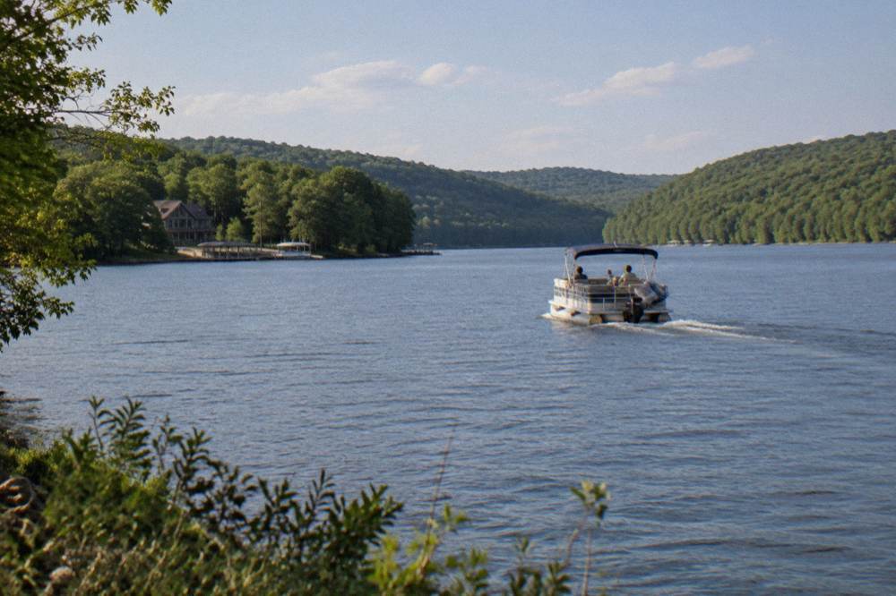 Pontoon boat cruising a wide section of open water between forested ridges