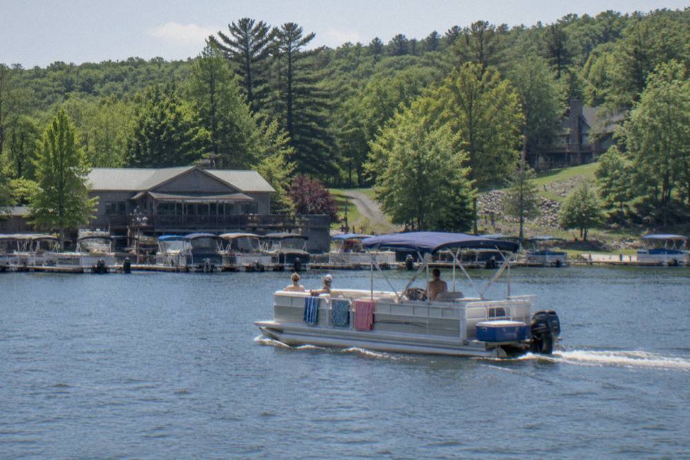 A rental pontoon boat cruising across open water with forested hills in the background