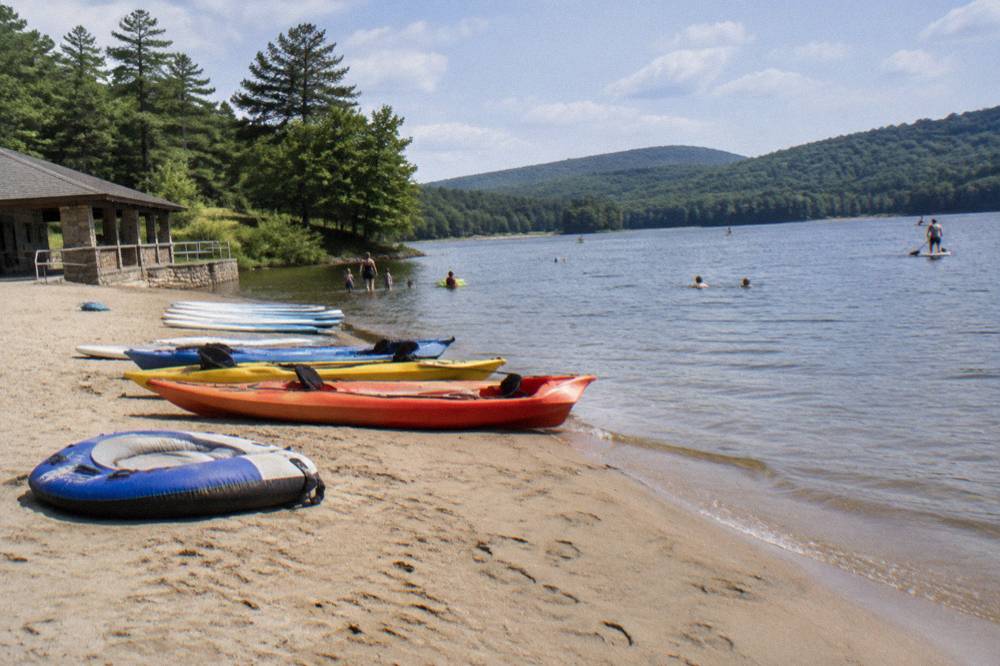 Kayaks and paddleboards lined up on a sandy beach beside calm lake water