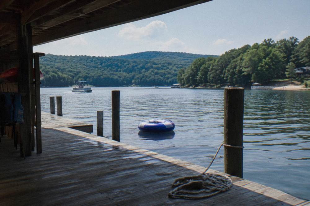 A wooden boat dock extending into a quiet cove with tree covered hills beyond