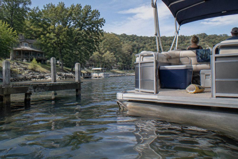A pontoon boat drifting on open water with tree covered ridges in the distance