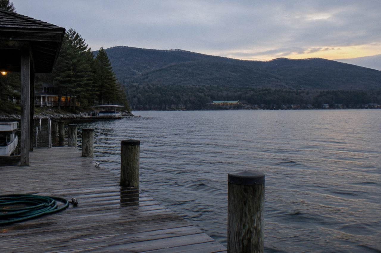 Calm lake water at dusk with forested hills along the shoreline and a small dock in the foreground