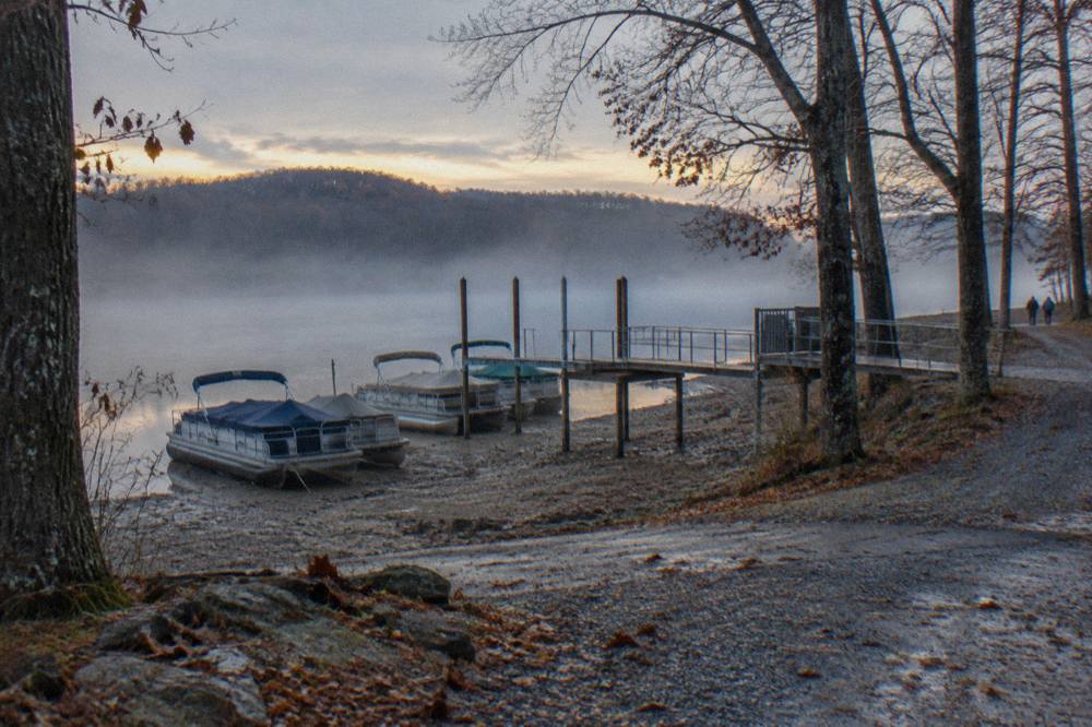 Empty pontoon boats tied at a dock on a calm lake morning with mist over the water
