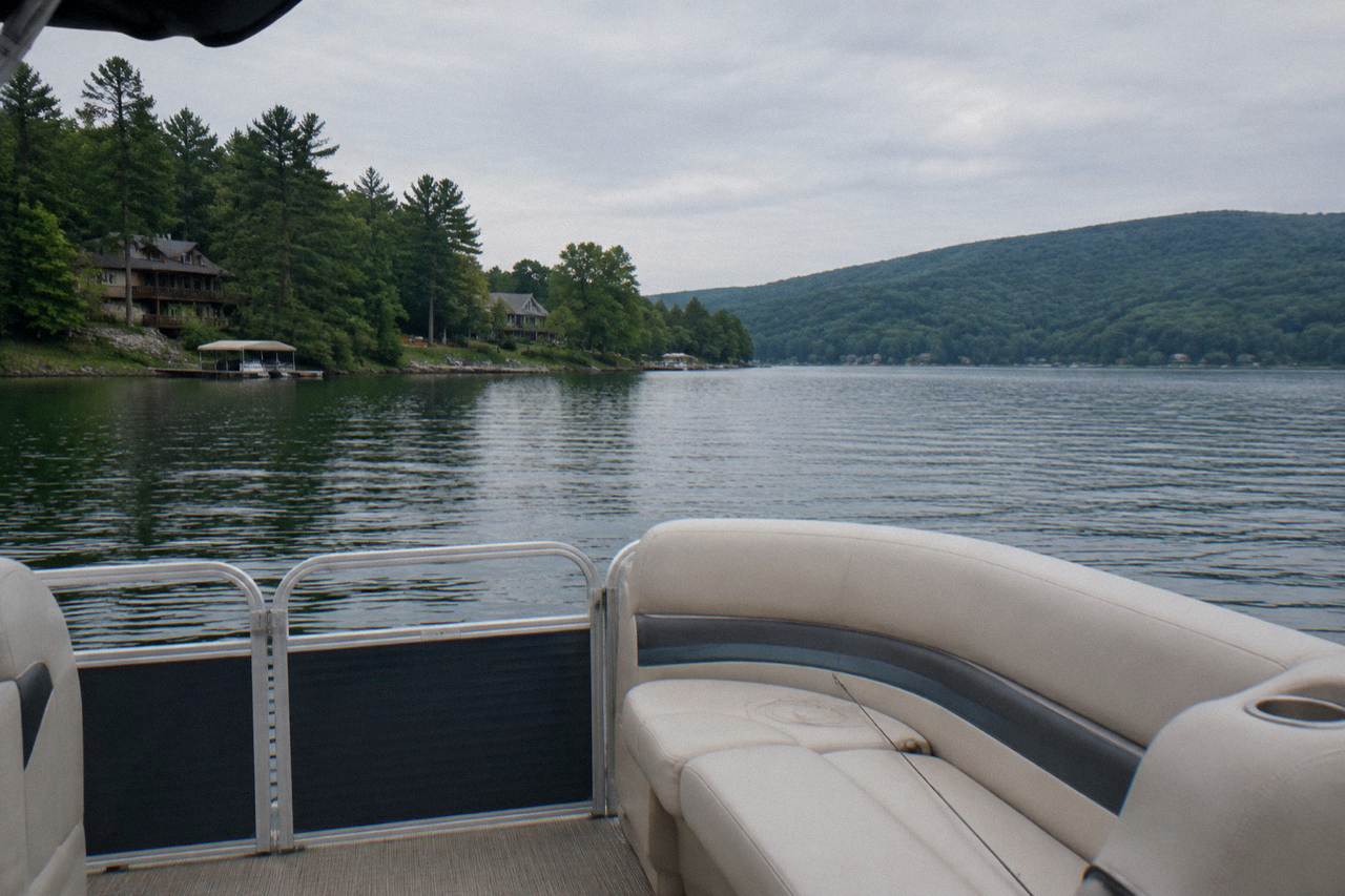Pontoon boat cruising calm open water on Deep Creek Lake with forested hills along the shoreline