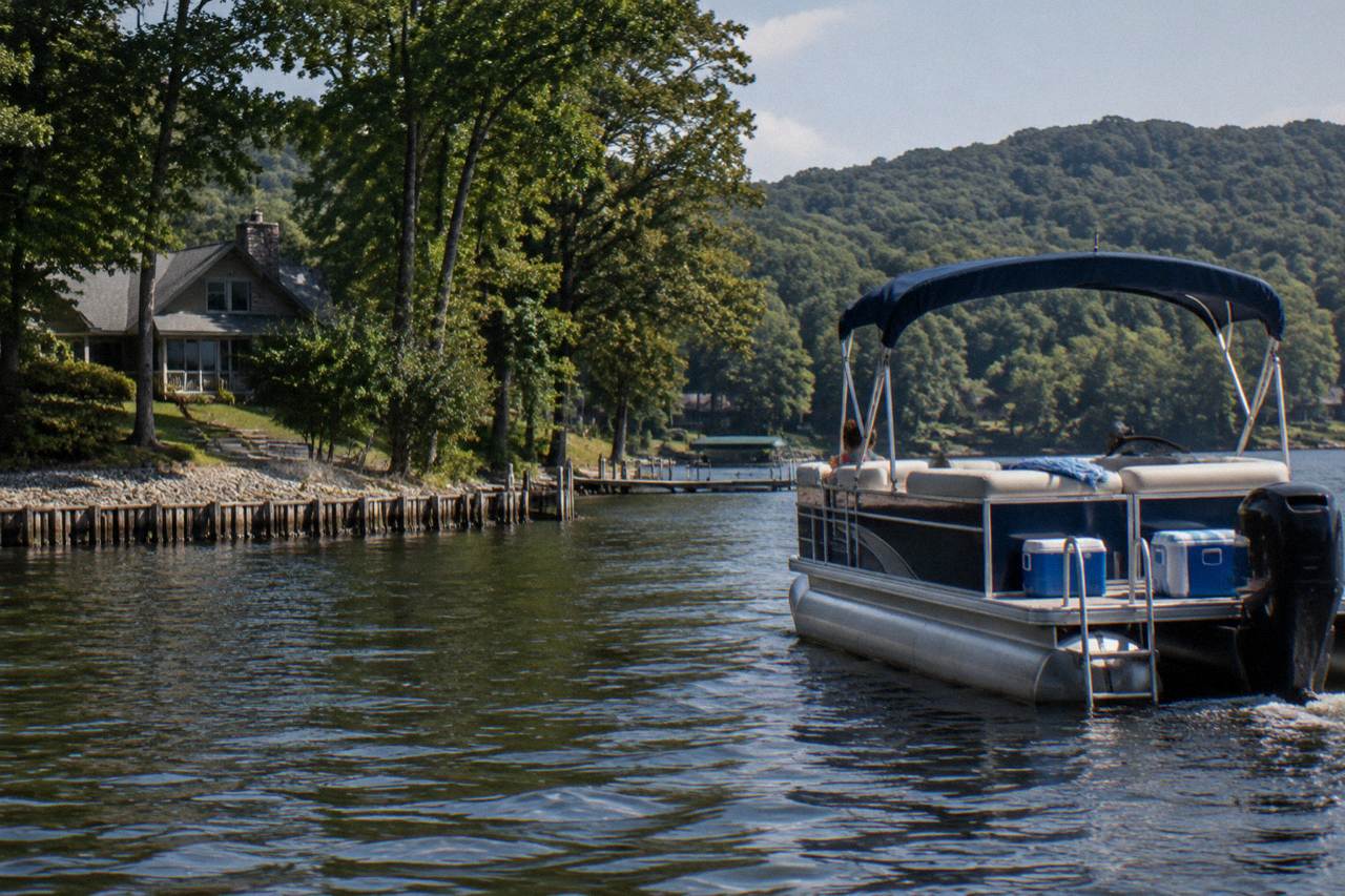 A pontoon boat cruising calm open water on Deep Creek Lake with forested ridges behind it