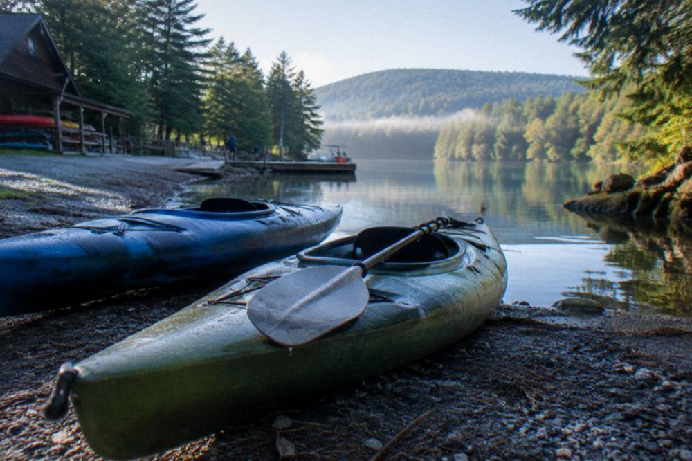 Kayaks resting on a gravel shore beside a wooded lake cove in morning light