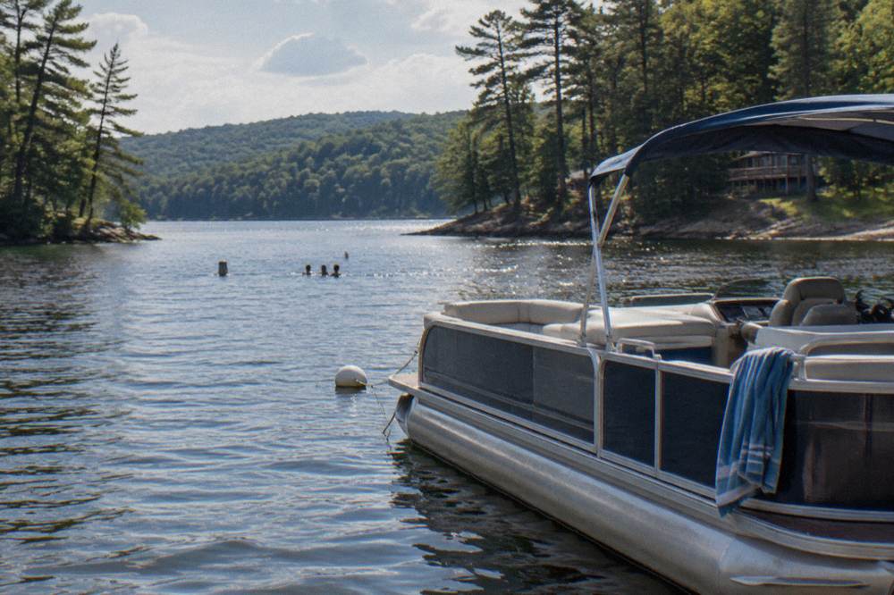 A family pontoon boat anchored in a quiet cove with tree-covered hills around the water