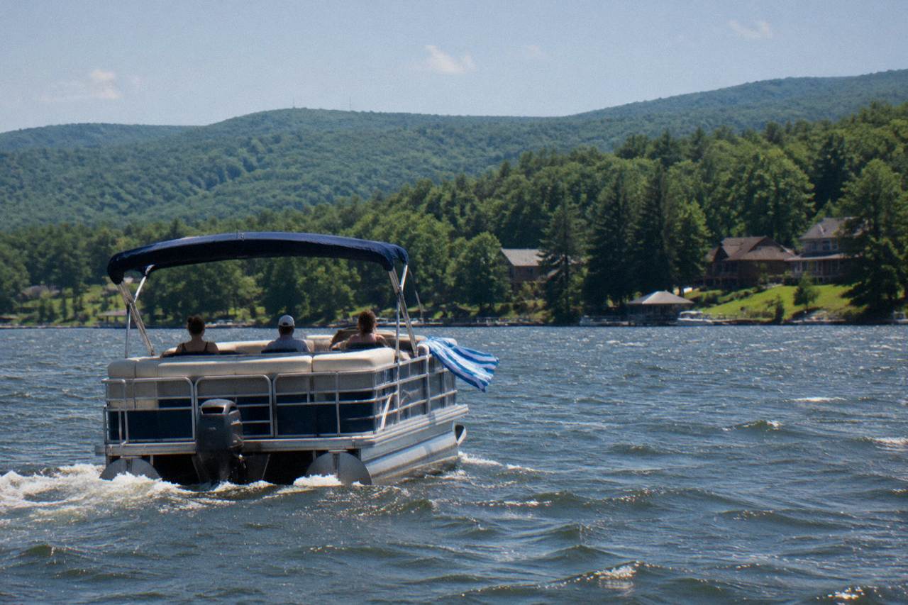 A pontoon boat cruising open water on Deep Creek Lake with forested hills behind it