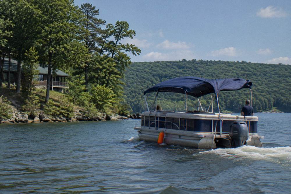 A covered pontoon tour boat passing a wooded point on the lake