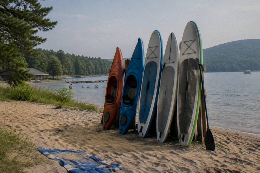 Paddleboards and kayaks lined up on a sandy beach beside calm water