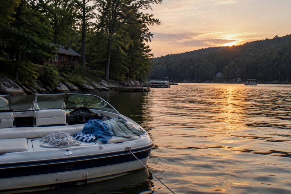 A boat anchored in a quiet cove with wooded hills in the background at dusk