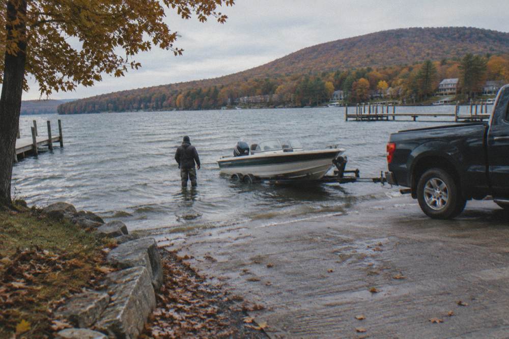Boat trailer backing down a public launch ramp toward calm water