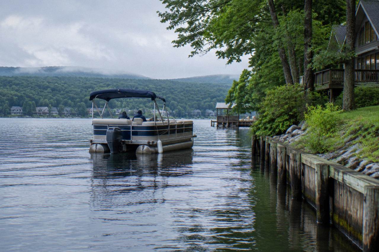 Pontoon boat cruising calm water along a wooded shoreline at Deep Creek Lake