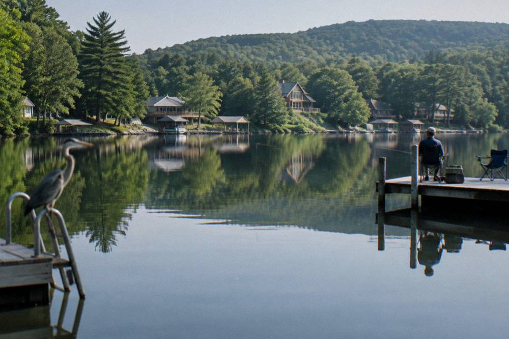 Tree-covered ridgeline reflected in still lake water near a shoreline of docks