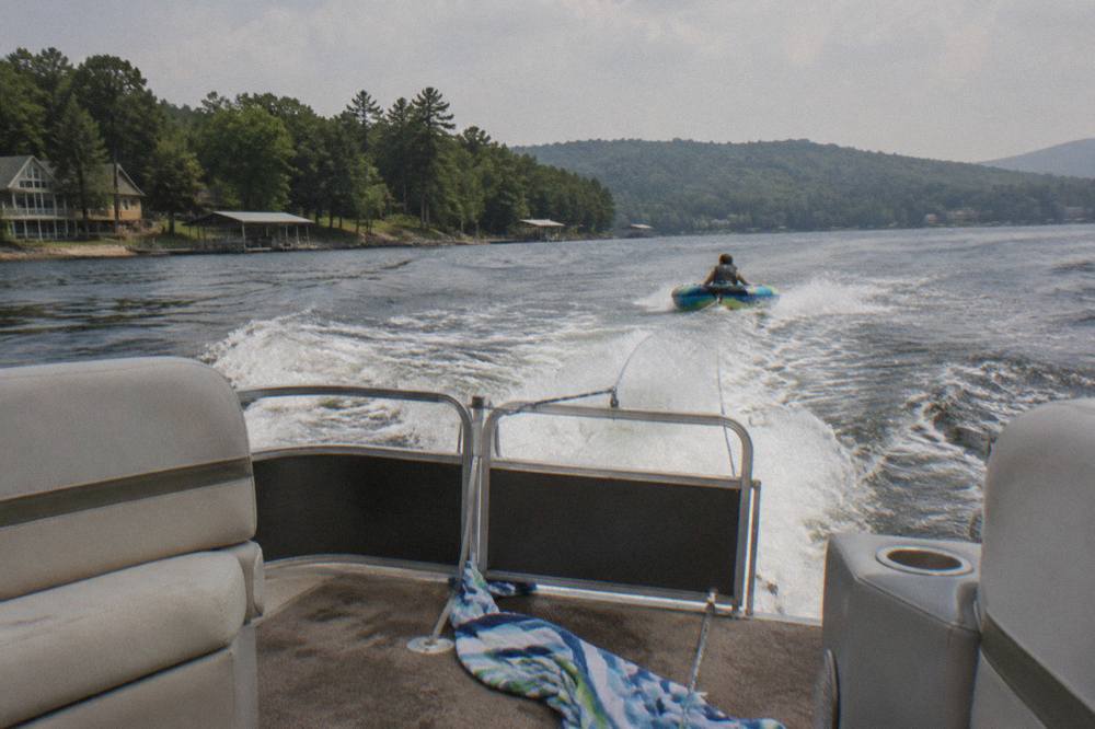 Tuber riding behind a pontoon boat on calm lake water