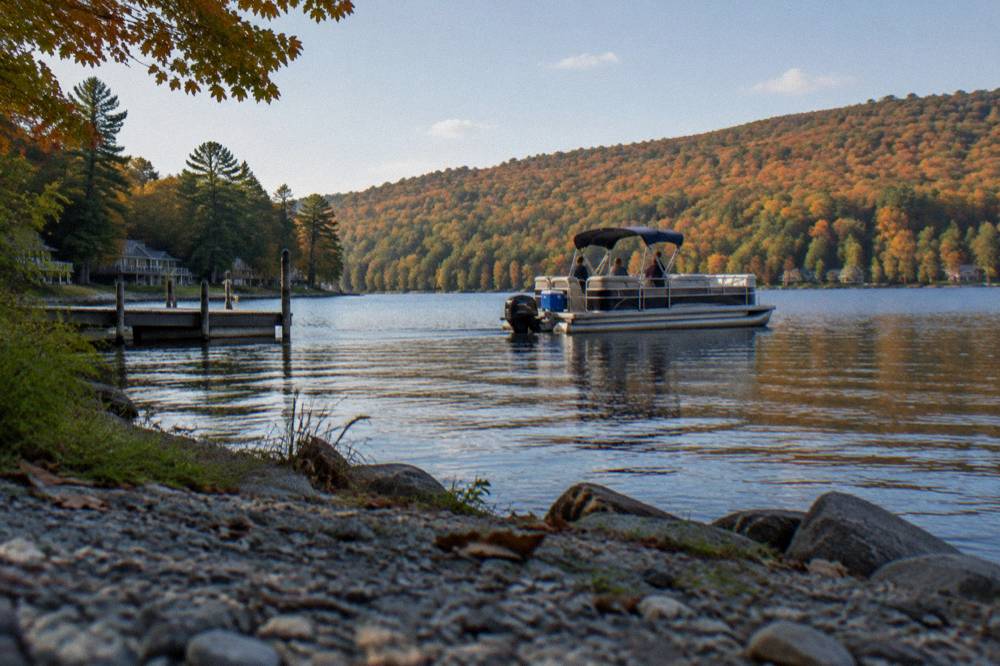 Pontoon boat on calm water in early fall with autumn color on the hills around the lake