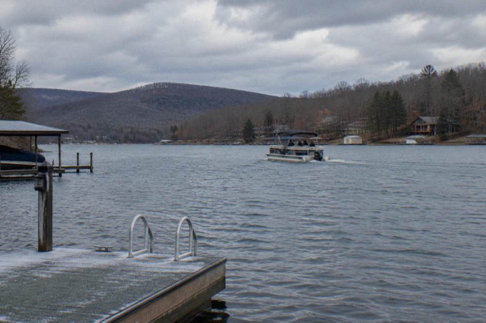 A pontoon boat cruising the open middle of a lake surrounded by autumn hills
