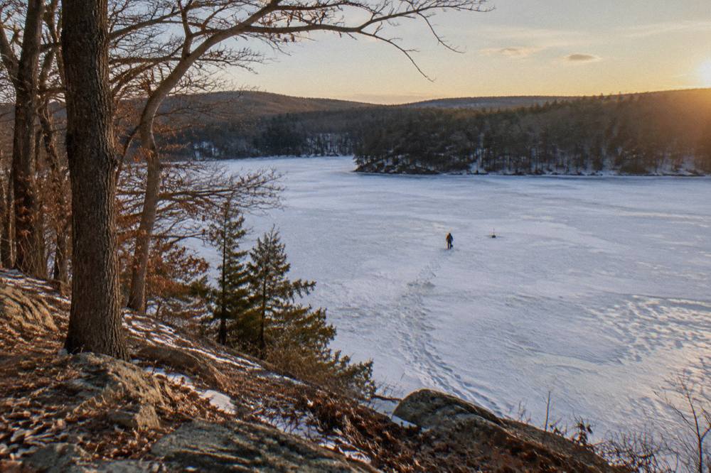 A snow-covered frozen lake with distant wooded shoreline under a pale winter sky