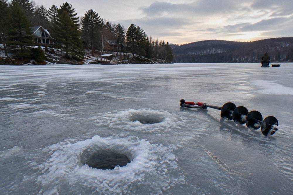 Ice fishing holes drilled in a frozen lake surface with a auger resting nearby