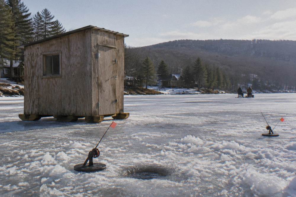 A ice fishing shanty on a frozen lake with rods set up beside an open hole