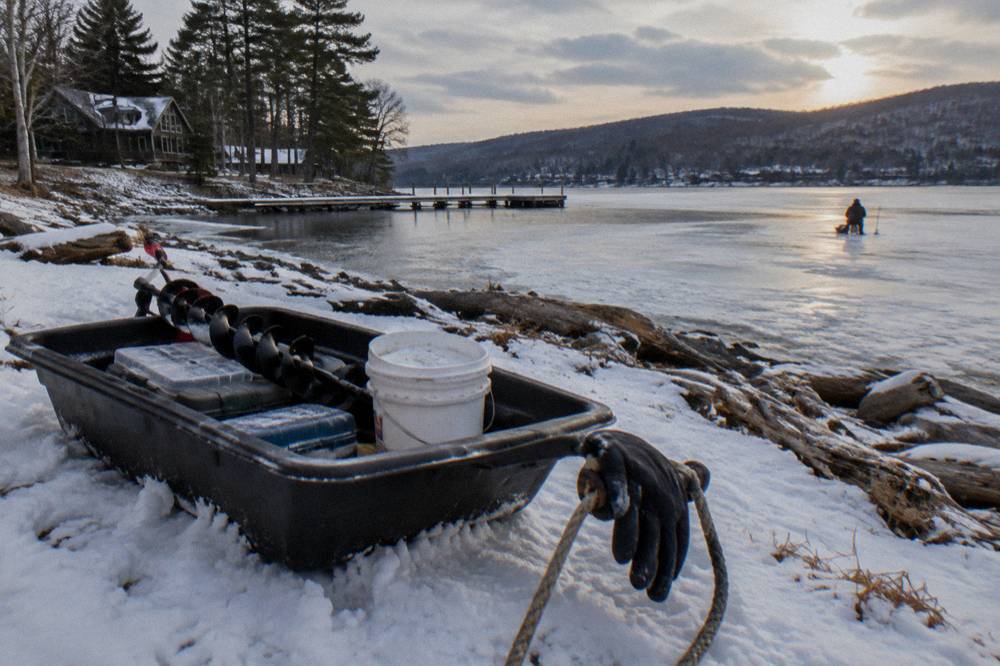 A sled loaded with ice fishing gear on snow beside a frozen lake shoreline