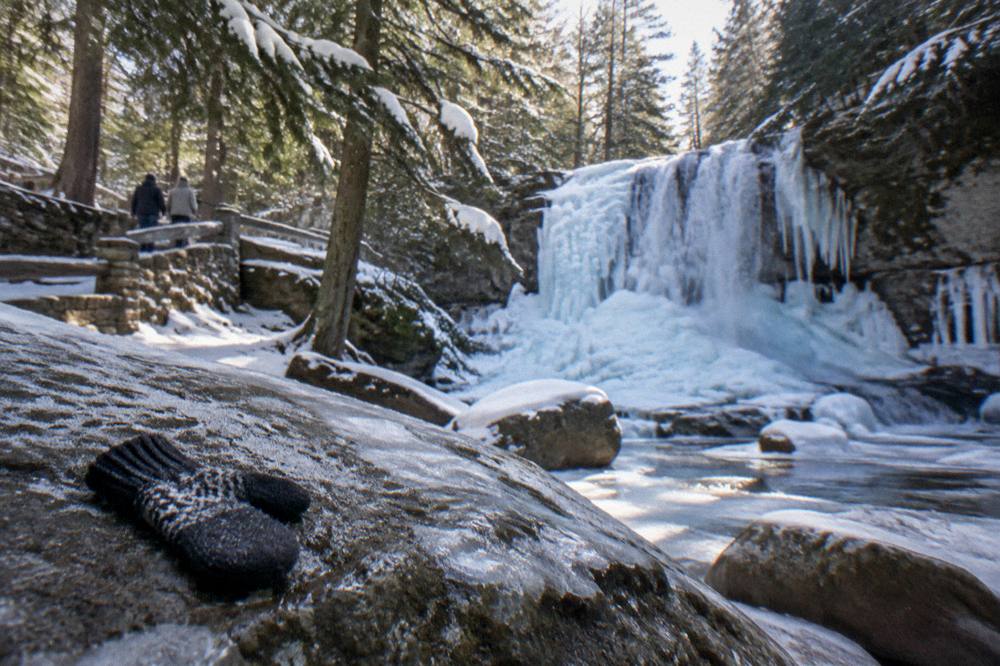 A frozen waterfall surrounded by ice-covered rocks and evergreen trees in winter