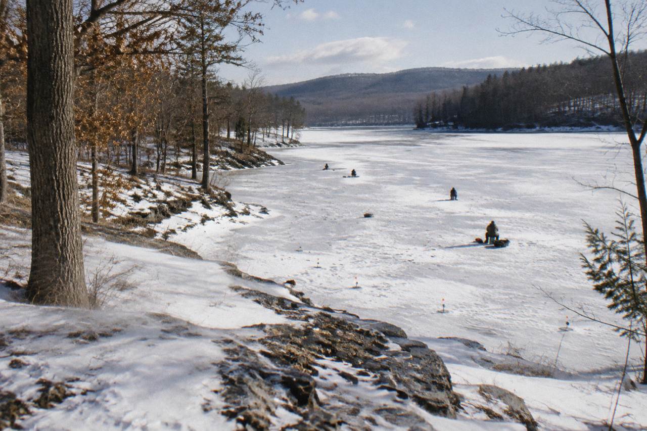 A frozen lake cove with snow-covered hills and bare trees at the shoreline