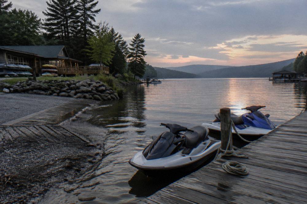 A dock on a lake with personal watercraft tied alongside and calm water stretching toward distant hills