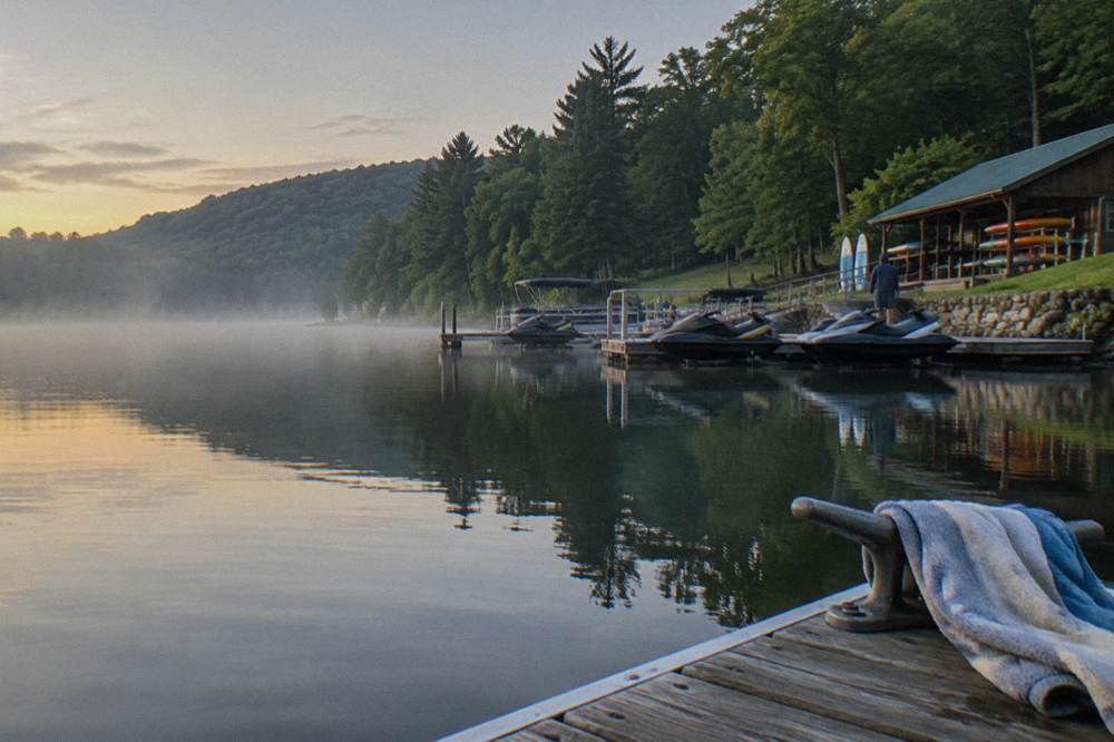 A calm cove at morning with mist over the water and forested hillsides reflected in the surface