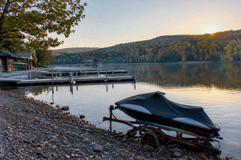 A lake shoreline in early fall with mixed green and golden trees and empty morning water