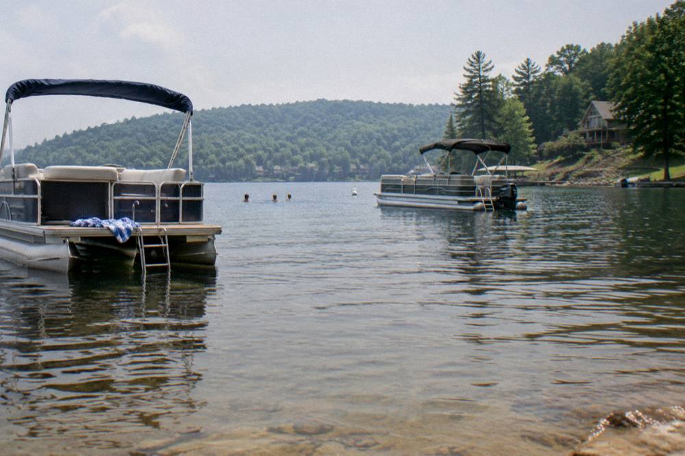 Anchored pontoon boats in a calm cove with forested hills around the water
