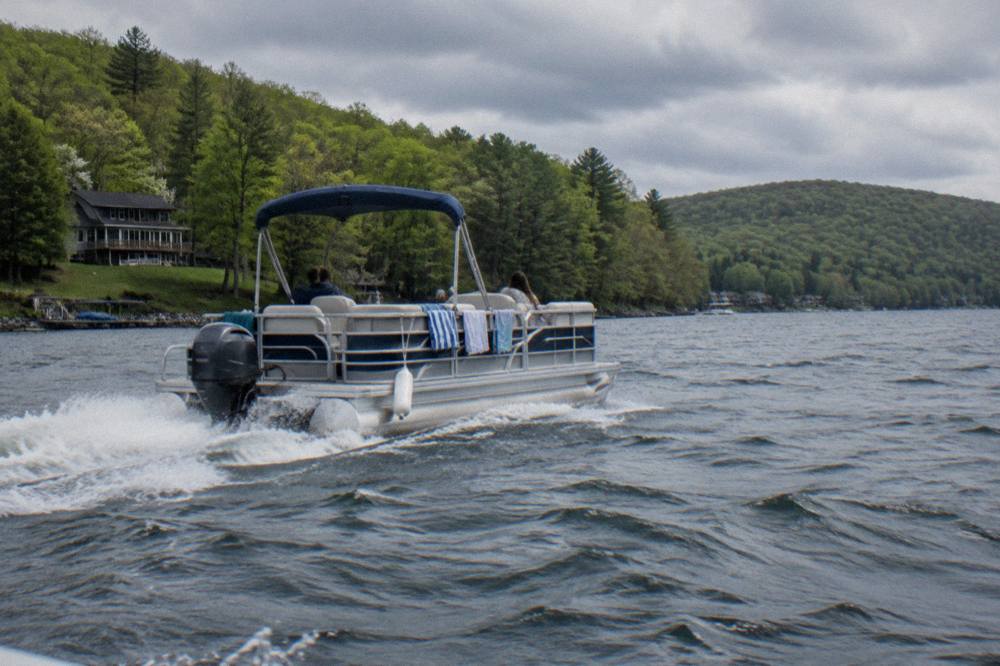 Pontoon boat cruising open water at Deep Creek Lake with forested hills behind