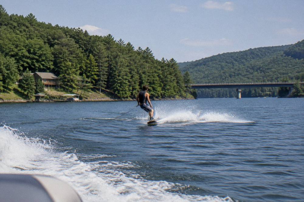 Wakeboarder carving across calm open lake water near a forested ridge